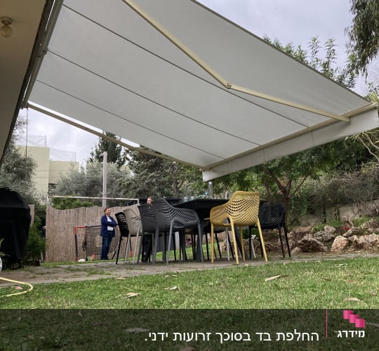 סוכך לבן מתוח מעל שולחנות וכיסאות בגינה
